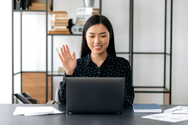 Vriendelijk schattig zelfverzekerde jonge aziatische vrouw freelancer, manager, ceo, zitten in het kantoor op laptop, praten via video gesprek met de klant of medewerkers, bespreken van zakelijke strategie, zwaaien hand, glimlachen — Stockfoto