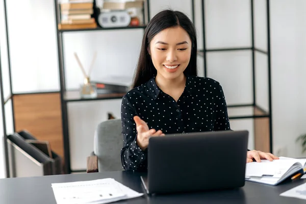 Karismatik sukses percaya diri wanita bisnis Asia, freelancer, manajer, menggunakan laptop, berbicara pada video konferensi dengan klien atau kolega, membahas proyek bisnis, memberi isyarat dengan tangan, tersenyum — Stok Foto