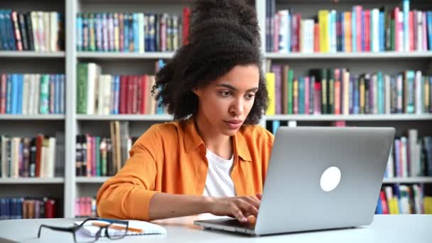 Emocionada chica estudiante afroamericana emocionada, vestida de moda, adolescente, escribiendo en el teclado, mira a la pantalla del ordenador portátil con sorpresa, cara sonriente, gesto con las manos, tiene una buena noticia o resultado — Vídeo de stock