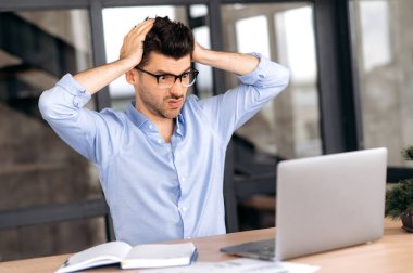 Kızgın Kafkas işadamı, komisyoncu ya da CEO, gözlük takıyor, ofiste çalışıyor, dizüstü bilgisayar kullanıyor, aşırı çalışıyor, stres yaşıyor, kafasının arkasında el ele tutuşuyor, sinir bozucu bir yönetici.