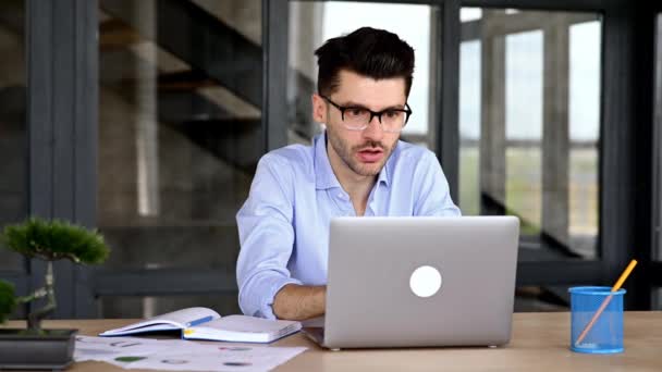 Empleado de oficina caucásico molesto, freelancer o corredor sentado en una mesa en una oficina moderna, mirando indignado a un ordenador portátil, sobrecargado de trabajo, estresado, gesto con las manos, gritando — Vídeos de Stock