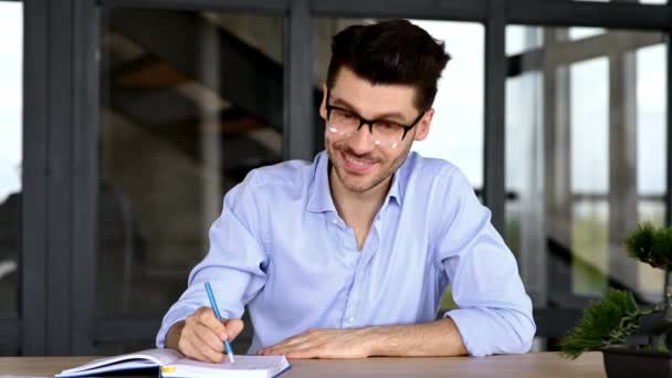 Uomo caucasico intelligente e fiducioso di successo, che prende appunti durante la consultazione online o l'apprendimento a distanza, ascolta l'interlocutore, comunica tramite videoconferenza, si siede alla scrivania — Video Stock