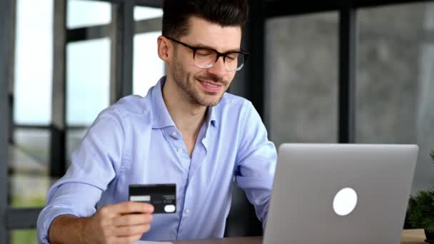 Online winkelen, betaling voor aankopen met creditcard en laptop. Blanke moderne man aan tafel gebruikt een laptop en een bankkaart om online aankopen of levering goederen thuis te betalen — Stockvideo