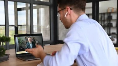 Online eğitim. Erkek serbest çalışanın ya da öğrencinin erkek öğretmenle bilgisayar ekranına çevrimiçi ders vermesi. Çevrimiçi uzaklık öğrenimi yapan adam, notlar alıyor, ekrana bakıyor.