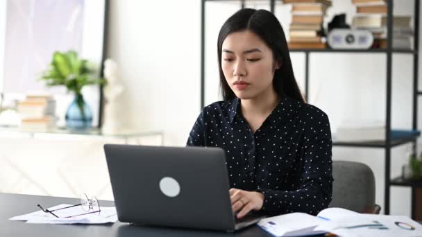 Confundido cansado, tensa mujer asiática freelancer o gerente, en camisa, se sienta en una mesa, utiliza el ordenador portátil, se toma un descanso, masajea sus sienes, mira a la pantalla con frustración, tiene estrés, necesita descanso — Vídeos de Stock