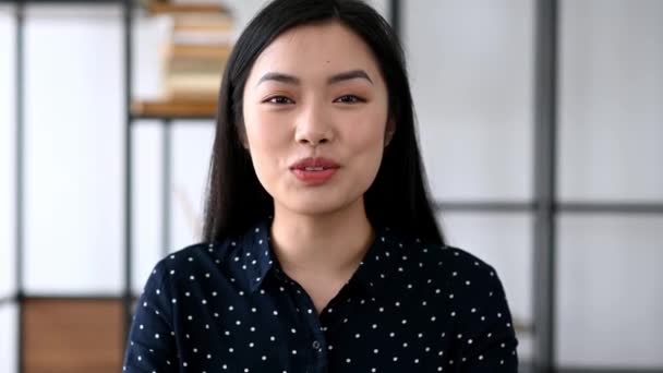 Comunicación a distancia. Amistosa mujer asiática joven bastante inteligente, freelancer o gerente, se sienta en el escritorio de trabajo, charlando con colegas o amigos a través de videollamada, saludando de la mano, sonriendo — Vídeo de stock