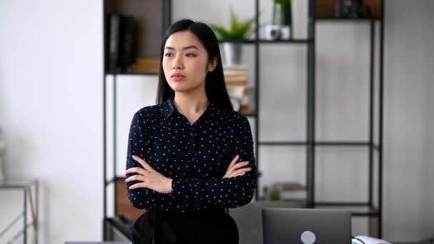 Positivo exitoso atractivo seguro joven asiático mujer de negocios o freelancer de pie cerca del escritorio con los brazos cruzados en la oficina, usando ropa formal con estilo, mira a la cámara, sonríe — Vídeo de stock