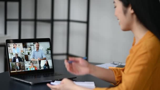 Videotelefonie, Online-Konferenz, Ferngespräche. Seitenansicht einer Chinesin, Studentin oder Freiberuflerin, sieht eine Online-Vorlesung, macht Notizen, multiethnisch lächelnde Menschen auf dem Computerbildschirm — Stockvideo