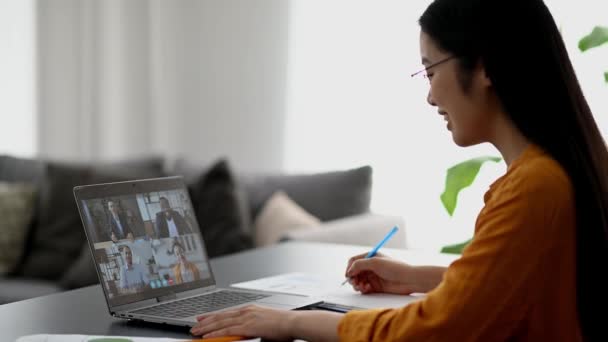 Videogesprek, online conferentie, afstandsonderwijs. Slimme Aziatische vrouwelijke student of freelancer, studeert of werkt op afstand, kijkt naar een online lezing, neemt notities, multiraciale mensen op laptop scherm — Stockvideo