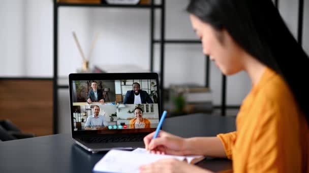 Videoconferência, aprendizagem à distância, trabalho online. Asiática bem sucedida estudante ou freelancer, estuda ou trabalha remotamente, assiste a uma palestra on-line, toma notas, pessoas multirraciais na tela do laptop — Vídeo de Stock