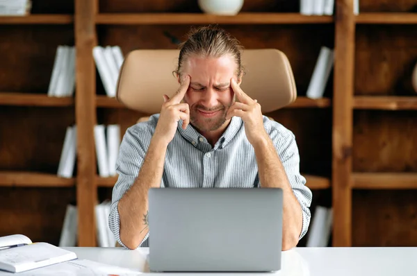 Υπερκόπωση νεαρός ενήλικας καυκάσιος υπάλληλος γραφείου, κάθεται σε ένα γραφείο στο γραφείο, κουρασμένος τύπος κάνει μασάζ στους κροτάφους του, κλείνει τα μάτια του, βιώνει πονοκέφαλο και ημικρανία, χρειάζεται ξεκούραση — Φωτογραφία Αρχείου
