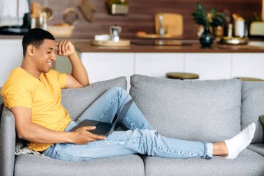 Evdeki kanepede oturan, dizüstü bilgisayar kullanan, internette gezinen, sosyal ağlarda sohbet eden, online alışveriş yapan, dizüstü bilgisayara bakan, gülümseyen,