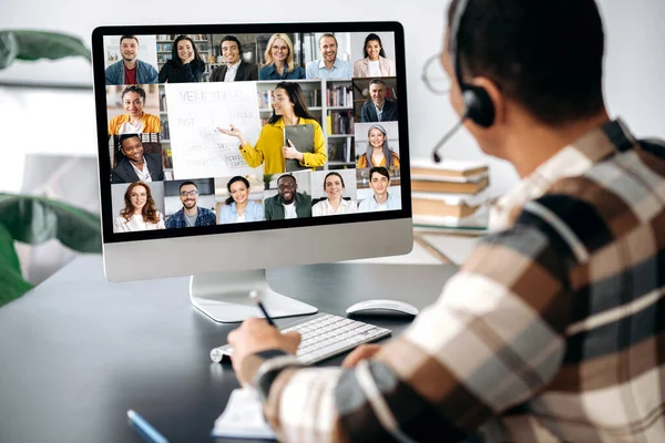 Distant learning, online education. View over a guys shoulder, a computer screen with multiracial people, female teacher conducts online lecture for students by video call, virtual meeting concept — Stock Photo, Image