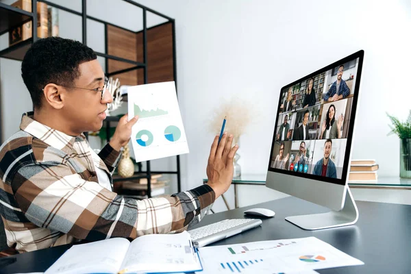 Virtual online meeting, distant negotiations. Latino young successful man, company worker, communicates with his multiracial business partners by video call, shows a graph, discuss strategy, project