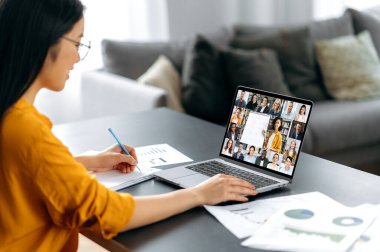 Öğretmen ve öğrencilerle video konferansı. Zeki Asyalı kız öğrenci çevrimiçi ders izliyor ve uzaktan çalışıyor. Genç bayan notlar alıyor, video konferansında bayan öğretmenden ders dinliyor.