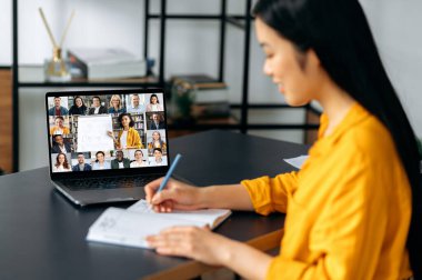 Online eğitim. Akıllı Japon öğrenci çevrimiçi izleme dersi alarak bilgi kazanıyor. Genç bir kadın, Webinar sırasında video konferansında notlar alıyor. Kadın öğretmen ve öğrenciler ekranda