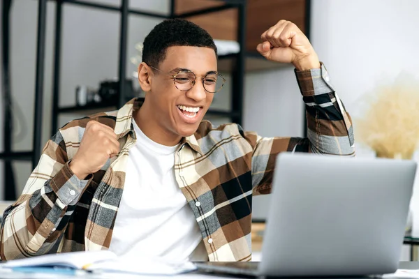 Feliz positivo exitoso joven hispano, vestido con estilo, oficinista, freelancer o diseñador se sienta en el escritorio, haciendo gestos con sus manos regocijándose en la victoria, el éxito, buen negocio, grandes ganancias —  Fotos de Stock