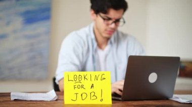 Odaklanamayan üzgün adam, öğrenci, işsiz, iş aramaktan bıkmış, masasında oturmuş, ne yazık ki yan tarafa bakıyor, masanın üzerinde iş arayan bir yazı var.