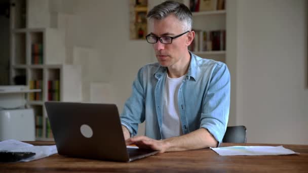 Hombre caucásico mayor de pelo gris agotado, gerente o freelancer, en ropa elegante, trabaja desde casa, cansado de muchas tareas, en el estrés, tomó un descanso del trabajo, necesita unas vacaciones, se frota los ojos con la mano — Vídeo de stock