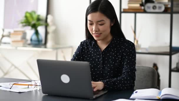 Feliz positivo bem sucedido asiático jovem mulher, elegantemente vestida, trabalhador de escritório, freelancer ou estudante senta-se na mesa de trabalho, gesticulando com as mãos se alegrando na vitória, sucesso, bom negócio, grande lucro — Vídeo de Stock