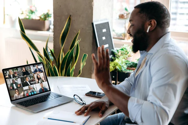 Віртуальна онлайн-зустріч за допомогою відео-дзвінка. Афроамериканець спілкується через відеоконференцію з багатонаціональними колегами, вітає співрозмовників, сидячи вдома на робочому місці, на віддаленій роботі. — стокове фото