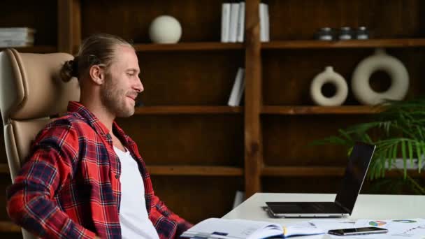 Bem-sucedido bonito amigável confiante jovem adulto caucasiano freelancer ou gerente com barba sentado à mesa, usando laptop, comunicação de vídeo com o cliente ou funcionários, acenando mão, sorrindo — Vídeo de Stock