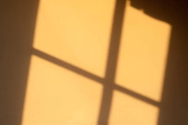 Shadow of a window in afternoon sun on a yellow wall