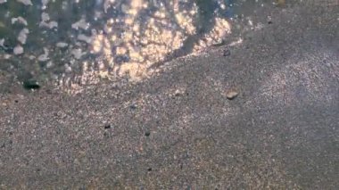 Deniz suyu sahile ulaşır, kumları kaplar, güneş suyun üzerinde parlar.