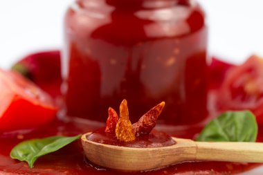 Tomato ketchup in a glass jar and green leaves on white . Homemade, healthy vegetarian food