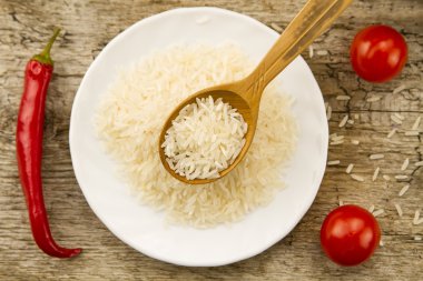 long grain rice in a wooden spoon on a background plates, chili pepper, cherry tomato. Healthy eating, diet, vegetarianism.