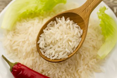 long grain rice in a wooden spoon on a background plate, green salad, chili pepper. Healthy eating, diet, vegetarianism.