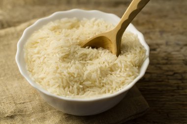 white plate of long grain rice with spoon on wooden background