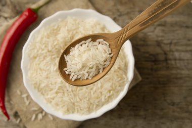 long grain rice in a wooden spoon on a background plates, chili pepper . Healthy eating, diet, vegetarianism.
