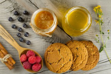 Blueberries and raspberries with cinnamon sticks and jars of honey with oat cookies on wooden background. Healthy vegetarian food, diet.
