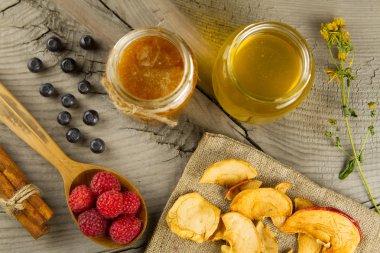Blueberries and raspberries with cinnamon sticks and jars of honey with dried apples on wooden background. Healthy vegetarian food, diet.