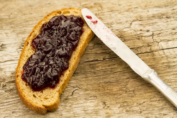 Pezzo di pane di segale con marmellata e coltello su fondo di legno — Foto Stock