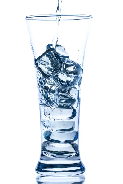 Pouring water in an elegant tall glass with ice and water drops on white background — Stock Photo, Image