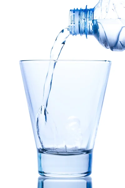Versando acqua in un elegante bicchiere e gocce d'acqua su fondo bianco — Foto Stock