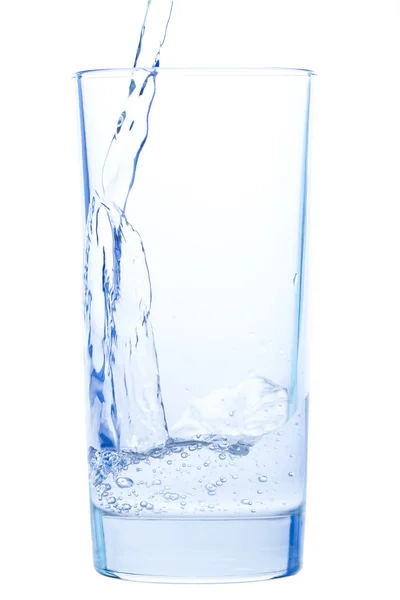 Versando acqua in un elegante bicchiere e gocce d'acqua su fondo bianco — Foto Stock