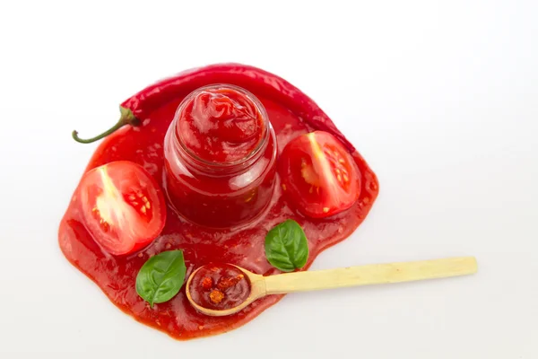 Tomato ketchup in a glass jar and green leaves on white . Homemade, healthy vegetarian food — Stock Photo, Image