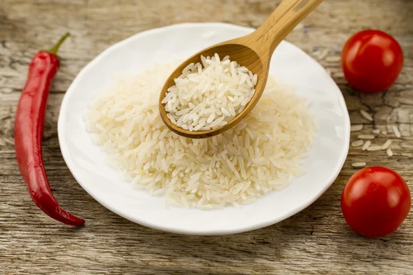 Long grain rice in a wooden spoon on a background plates, chili pepper, cherry tomato. Healthy eating, diet, vegetarianism. — Stock Photo, Image