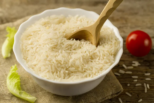 white plate of long grain rice with a spoon, cherry tomato, green lettuce on wooden background