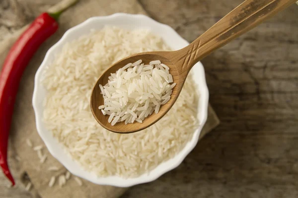 Long grain rice in a wooden spoon on a background plates, chili pepper . Healthy eating, diet, vegetarianism. — Stock Photo, Image