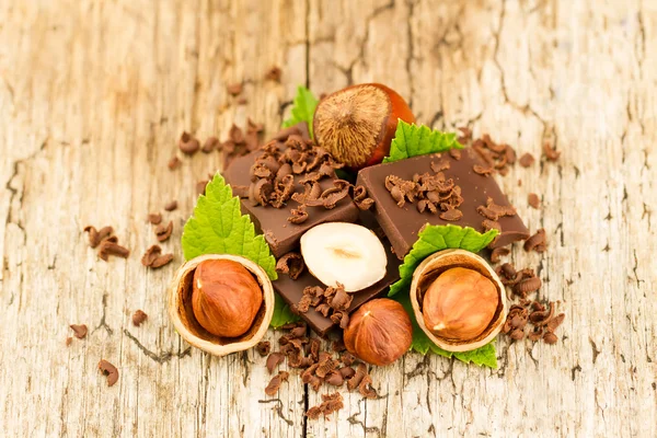 Hazelnoot met chocoladerepen en groene bladeren op oude houten achtergrond — Stockfoto