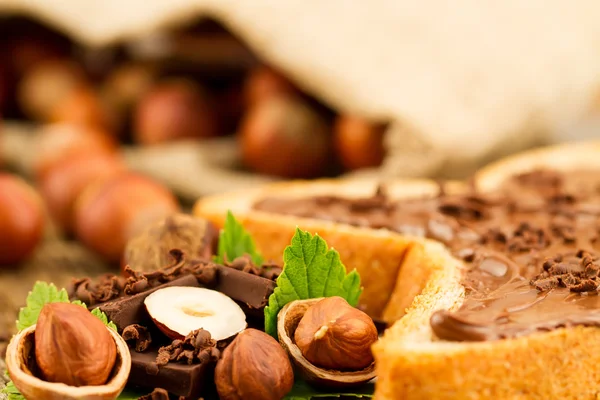 Hazelnut with chocolate, toast and green leaves on old wooden background — Stock Photo, Image