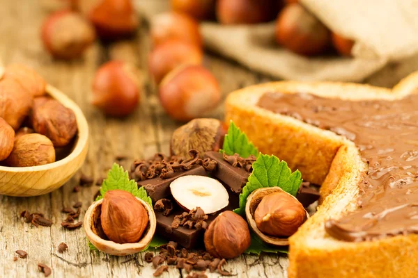 Hazelnut dengan coklat, roti panggang dan daun hijau pada latar belakang kayu tua — Stok Foto
