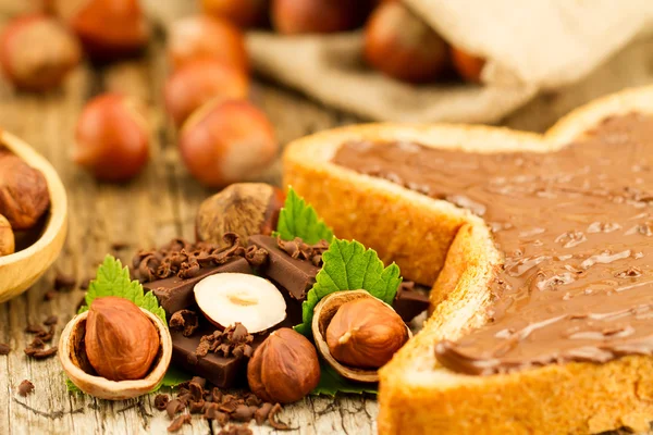 Hazelnut with chocolate, toast and green leaves on old wooden background — Φωτογραφία Αρχείου