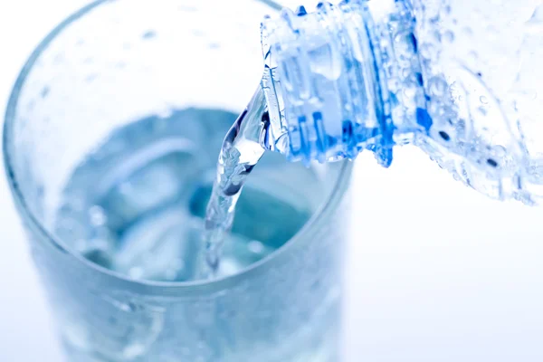 Versando acqua in un elegante bicchiere con ghiaccio e gocce d'acqua. Macro Fotografia Stock