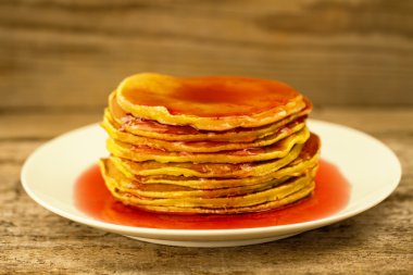 a stack of pancakes on a white plate with jam on wooden background