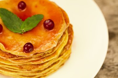 a stack of pancakes on a white plate with berries and jam on wooden background